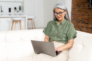 Picture of an older woman sitting on a couch and talking to a therapist through her laptop.